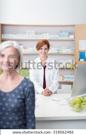 Elderly lady walking away from a smiling friendly attractive young female pharmacist after being served with her medication, focus to the pharmacist
