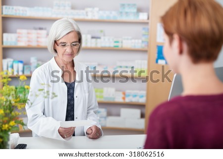 Senior lady pharmacist assisting a patient with prescription medication standing behind the counter reading the script