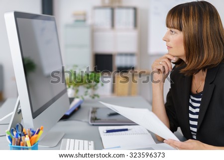 Side View of a Businesswoman Looking at her Computer Screen Seriously While Holding Documents.