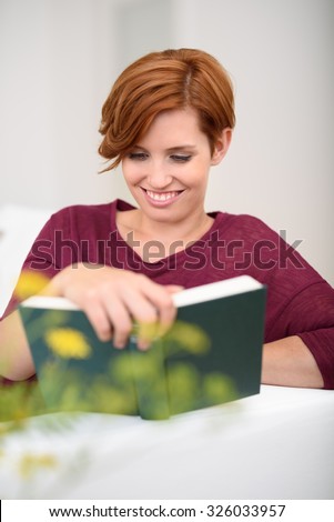Pretty Young Woman Reading a Book with Happy Facial Expression While Relaxing at the Couch in the Living Room
