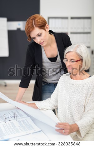 Middle Aged And Young Office Women Reading Business Documents at the Table Inside the Office.