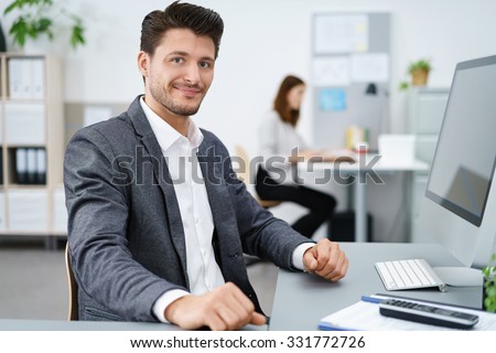 manager sitting at desk and working on computer with co-worker in background