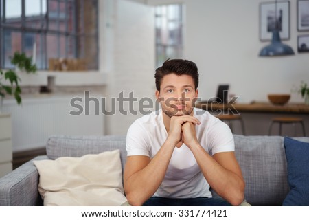 relaxed young man leaning chin on hands while sitting on his sofa at home