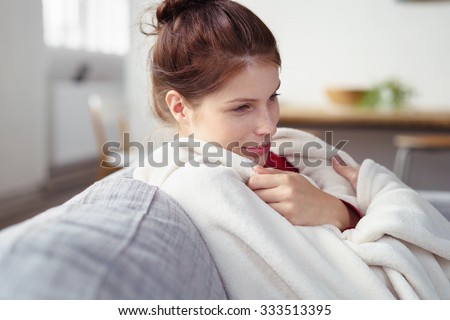 woman snuggling into a warm blanket while sitting on her sofa with a dreamy smile