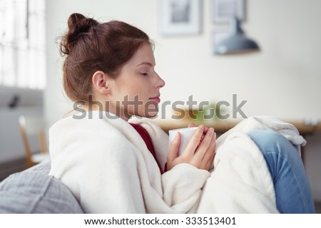 woman holding a cup of warm tea while relaxing on the sofa with eyes shut