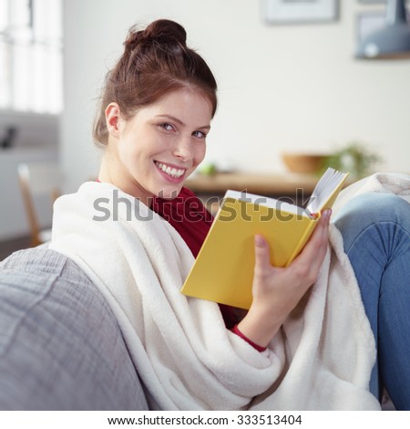 woman reading a book at home wrapped in a soft white blanket