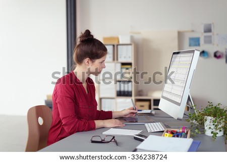 Stylish businesswoman working on a desktop computer sitting in profile reading information on the screen