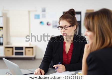 Two serious businesswomen in a meeting sitting together at a desk discussing information on a laptop computer