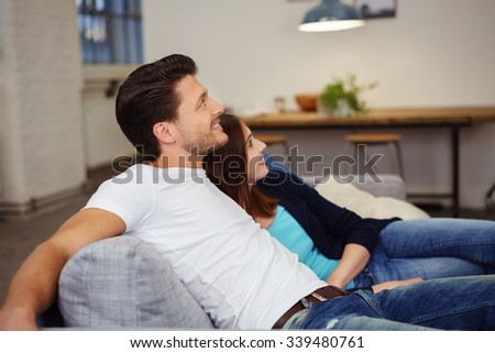casual couple relaxing on the sofa with arms around each other looking up with a smile
