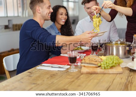 Happy Young Man Holding his Plate While Someone is Dishing Up for Him During Dinner.