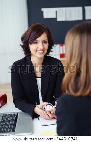 Smiling Young Businesswoman Talking to her Female Co-worker at her Desk Inside the Office.