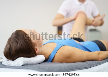 Injured Young Woman Lying on a Therapy Bed While her Personal Physical Therapist is Massaging her Leg.