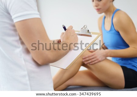 Physical Therapist Recording the Knee Condition of a Female Patient on a Paper Inside the Clinic.