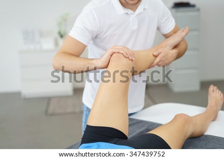 Professional Physical Therapist Lifting the Injured Leg of a Patient and Massaging it Slowly.