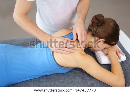 Physical Therapist Massaging the Back and Shoulder of a Female Patient, Lying Prone on the Bed.