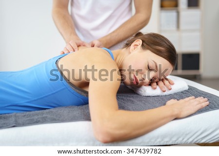 Young Woman Lying in Prone Position, with One Arm on the Side, While her Physical Therapist is Giving a Massage on her Injured Upper Back.