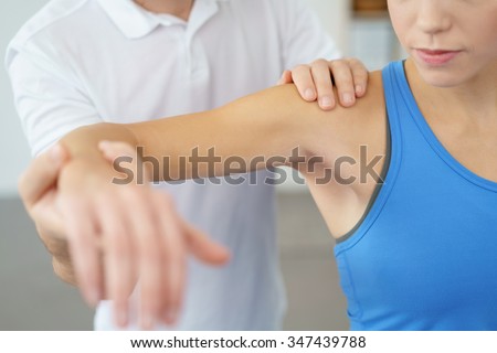 Close up Professional Physical Therapist Lifting the Arm his Female Patient While Examining the Injured Shoulder.