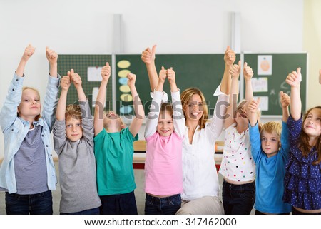 Happy Teacher and Kindergarten Students Showing Thumbs Up Overhead Inside the Classroom.