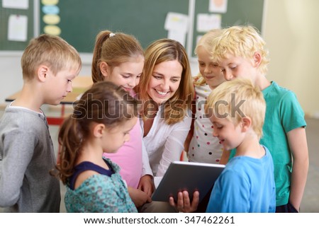 Cheerful Female Teacher with her Young Students Watching a Video on a Tablet Computer Together Inside the Classroom.