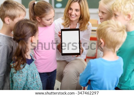 Cheerful Female Teacher Showing a Tablet Computer with Blank Screen While Teaching the Kids Inside the Classroom.