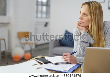 Woman with Laptop and Paperwork making Some Notes at her Table at home