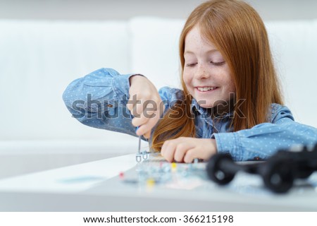 Pretty little redhead girl sitting at a table at home working with a screwdriver with a beaming smile