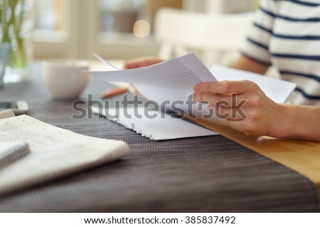 Person seated at a table with a cup of coffee reading a paper document, close up view of the hands