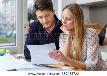 Handsome young man with mustache and beautiful woman with long hair at table looking at documents in kitchen next to window