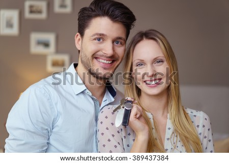 Happy excited young couple with keys to a new home or apartment standing grinning happily at the camera, close up head and shoulders