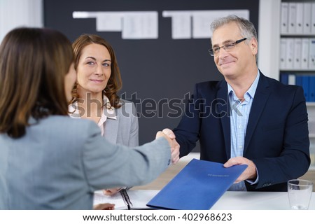 Businessman and woman conducting an interview smiling as they congratulate and shake hands with the prospective applicant while holding her CV