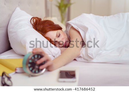 Young woman reaching out for her alarm clock to switch it off as it wakens her in the morning from a restful sleep
