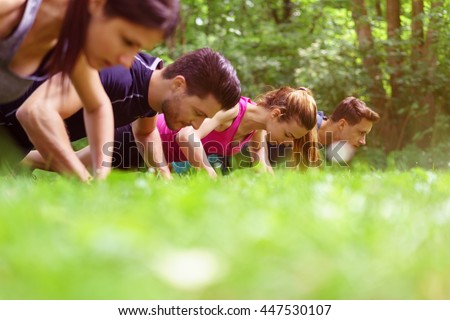 Two young couples working out doing push-ups outdoors in a park with an extreme low angle view across the top of the grass of their heads and shoulders