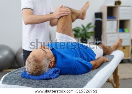 Physiotherapist working with an elderly patient doing mobility and functionality exercises with his left knee as he lies in an examination couch