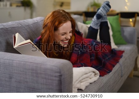 redhead woman laughing while reading a funny book