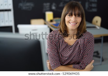 Attractive businesswoman with a friendly welcoming smile leaning forwards on her desk looking directly at the lens