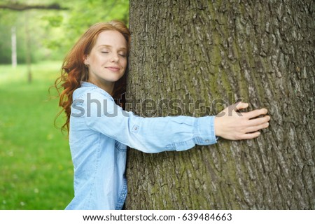 Contented young woman hugging a large tree with a blissful expression and her eyes closed in a concept of nature conservation