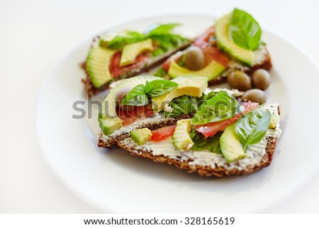 Healthy sandwich with whole-grain bread, avocado, tomato, basil leaves and olives on plate; healthy eating; organic food;