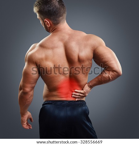 Muscular man with back pain over gray background. Concept with highlighted glowing red spot.