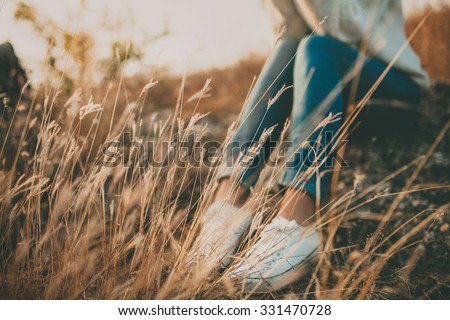 Defocused abstract loneliness concept. Cropped feet of lonely young woman sitting on stone. Solitude