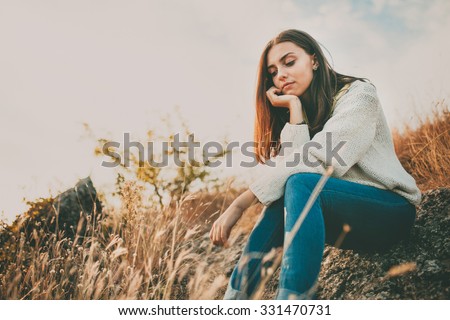 Sad young girl sitting alone on a stone outdoors. Teenage girl thinking thoughtfully. Hope. Sadness. Loneliness