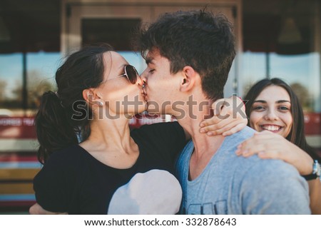 Loving couple of teenagers kissing while their friend watching. Hipsters love. Young man kissing his girlfriend.