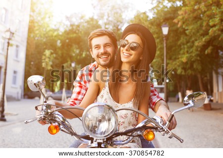Young and carefree couple learning to drive a scooter on a road. Young man is teaching hipster girl to ride a motorcycle.