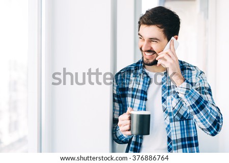 Young man wearing casual clothes talking on a mobile phone in the morning at a window with copy space,