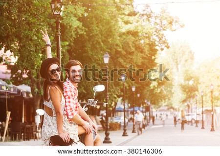 glamorous happy young couple riding  a vintage scooter in the street, woman wears a hat and sunglasses