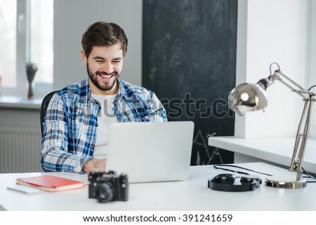 Happy young man sitting in office and using laptop computer, smiling, chatting online. Handsome man having a video conversation