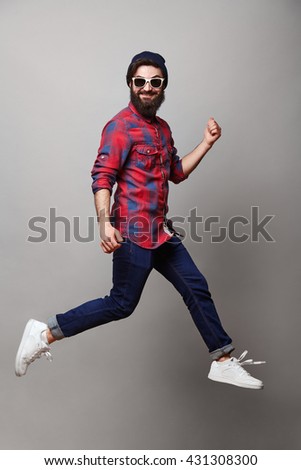 happy excited jmping young bearded man. Funny portrait on young casual male model in humorous jump on grey background.
