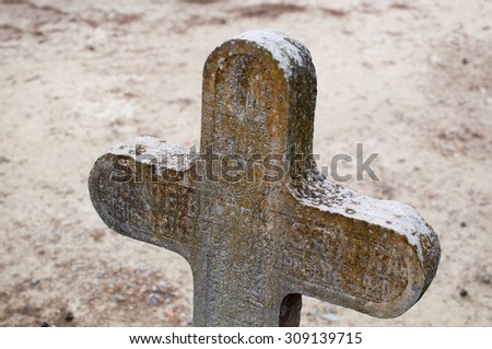 Old cross in a cemetery with moss on top.