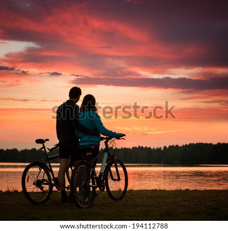 Romantic Couple with Bicycles Watching Sunset. Summer Nature Background with Beautiful Clouds, Sky and River. Active Leisure Concept.