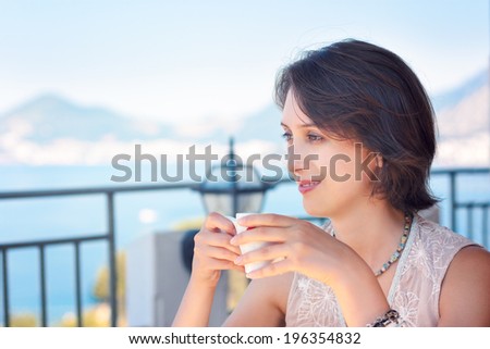 Portrait of Smiling Young Woman Drinking Coffee at Cafe Terrace. Sea Summer Vacation Concept. Copy Space.