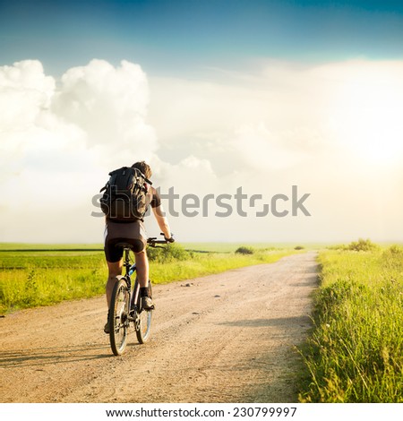Rear View of a Man with Backpack Riding a Bicycle on Beautiful Nature Background. Healthy Lifestyle and Travel Concept. Instagram Styled Toned Photo. Copyspace.